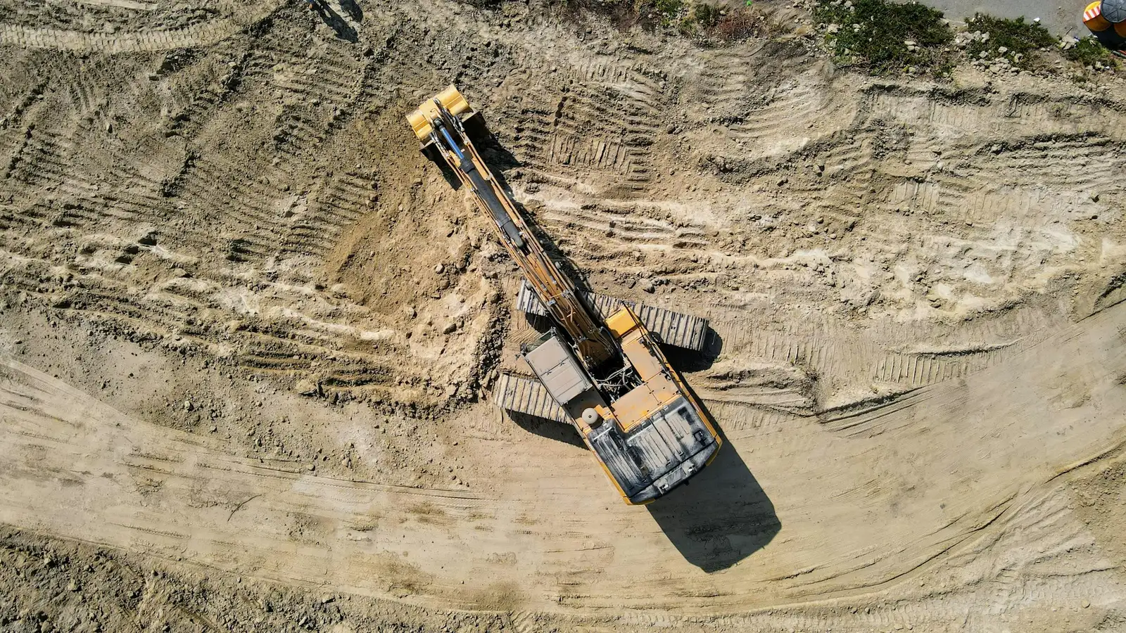 An excavator seen from above, digging in a sandy excavation