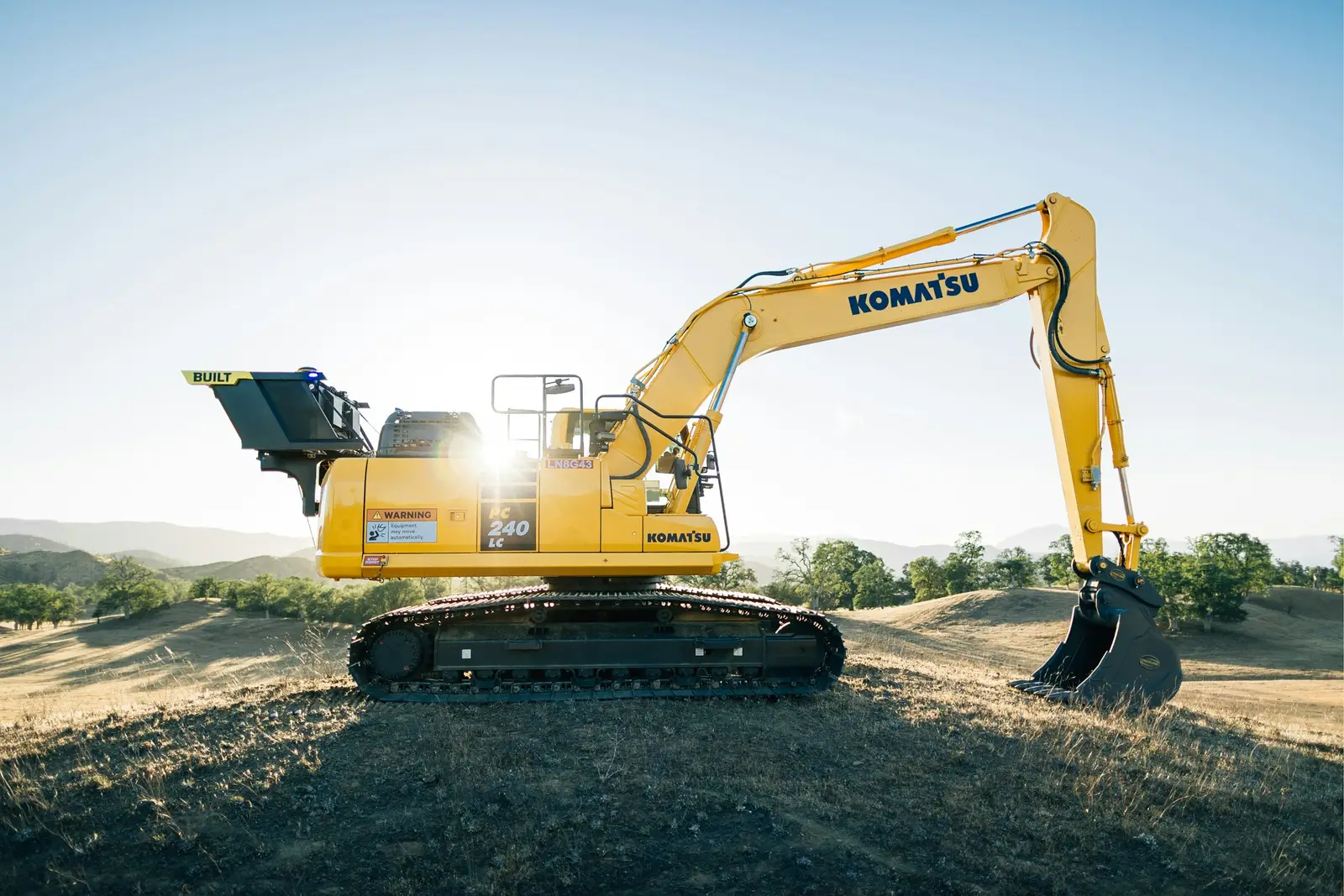 A yellow tracked excavator on open ground in low sun