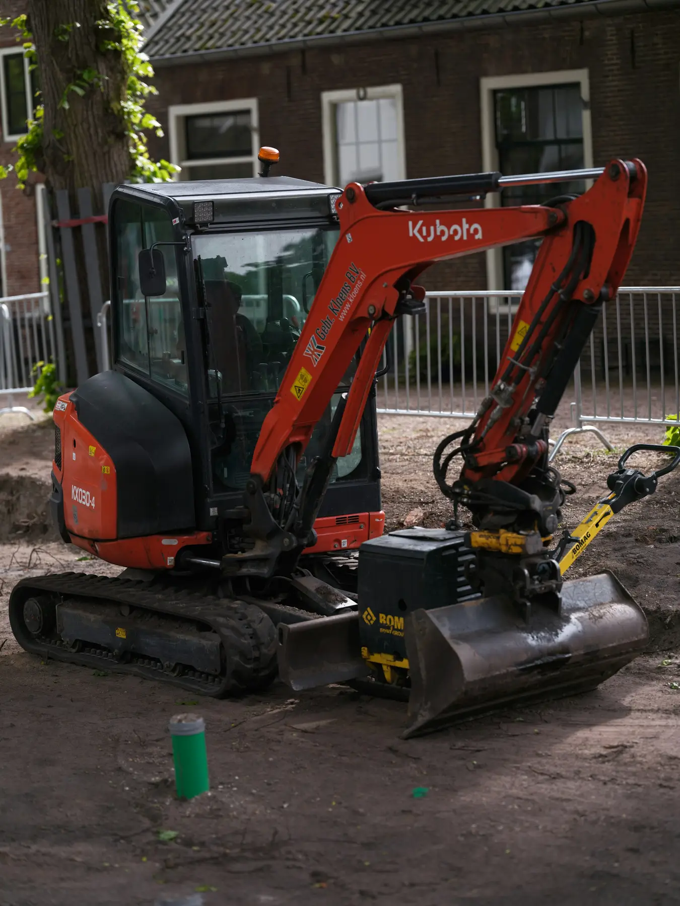A red mini digger on a site beside brick houses