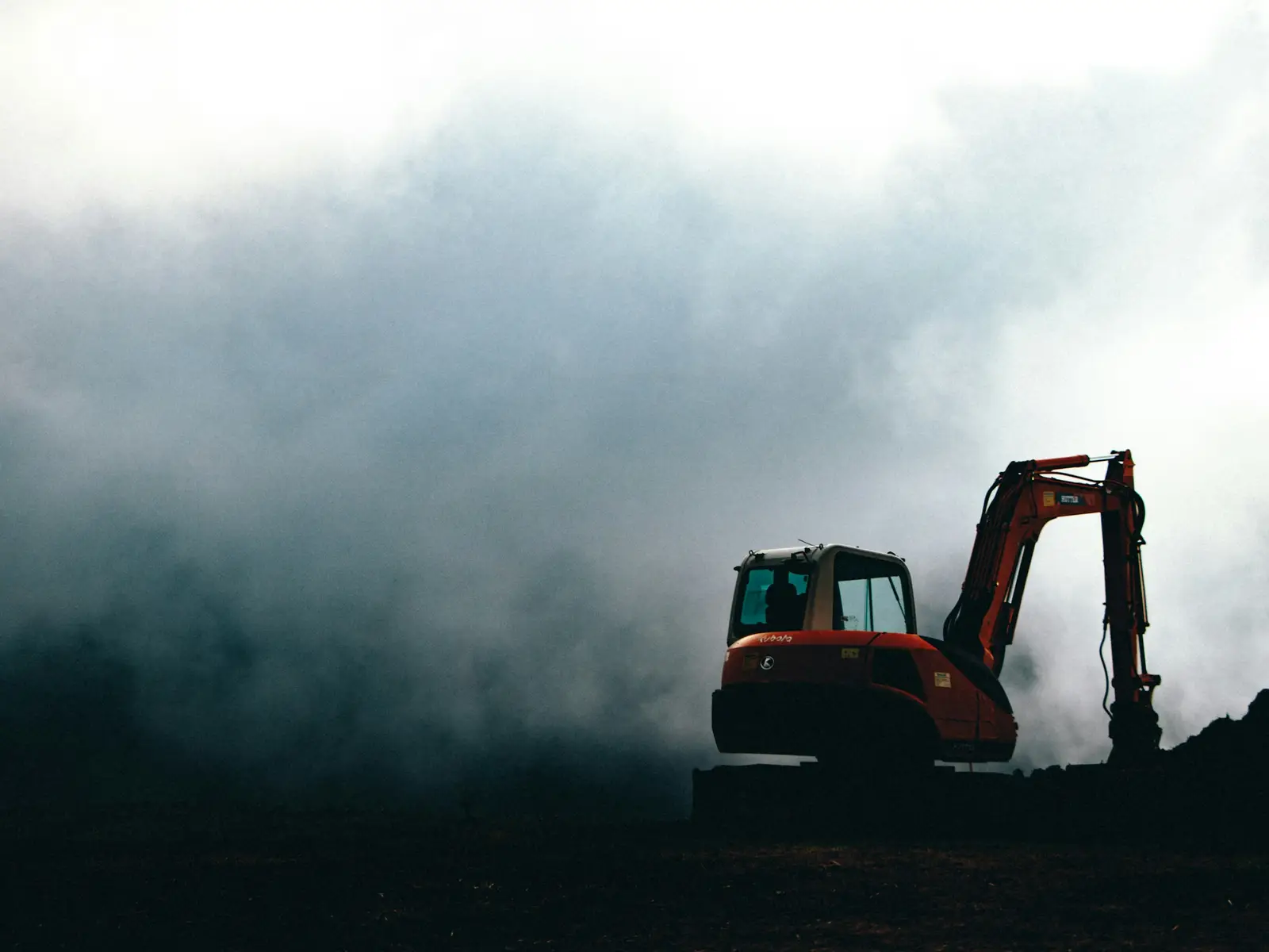 A small excavator on a mound, in silhouette against mist