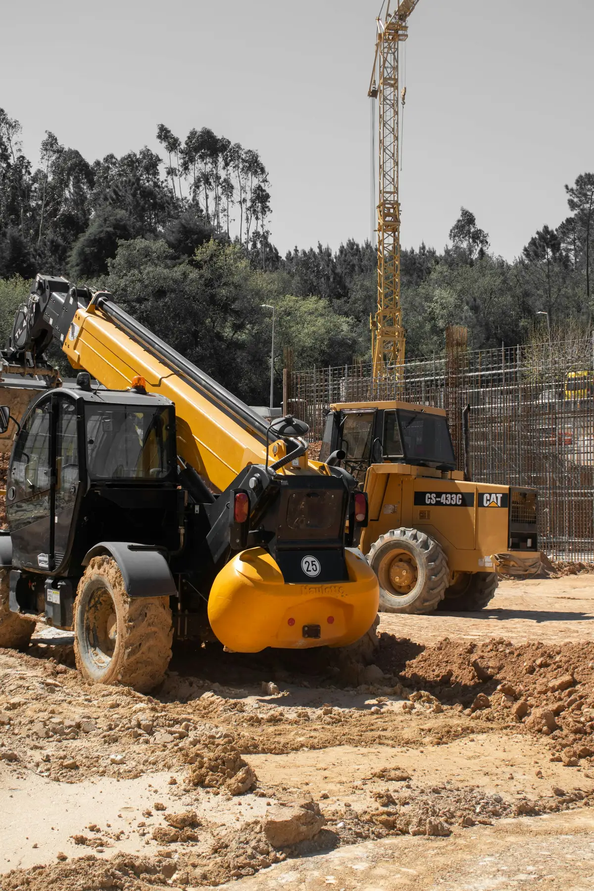 A telehandler and a site dumper on a muddy building site, with a tower crane behind