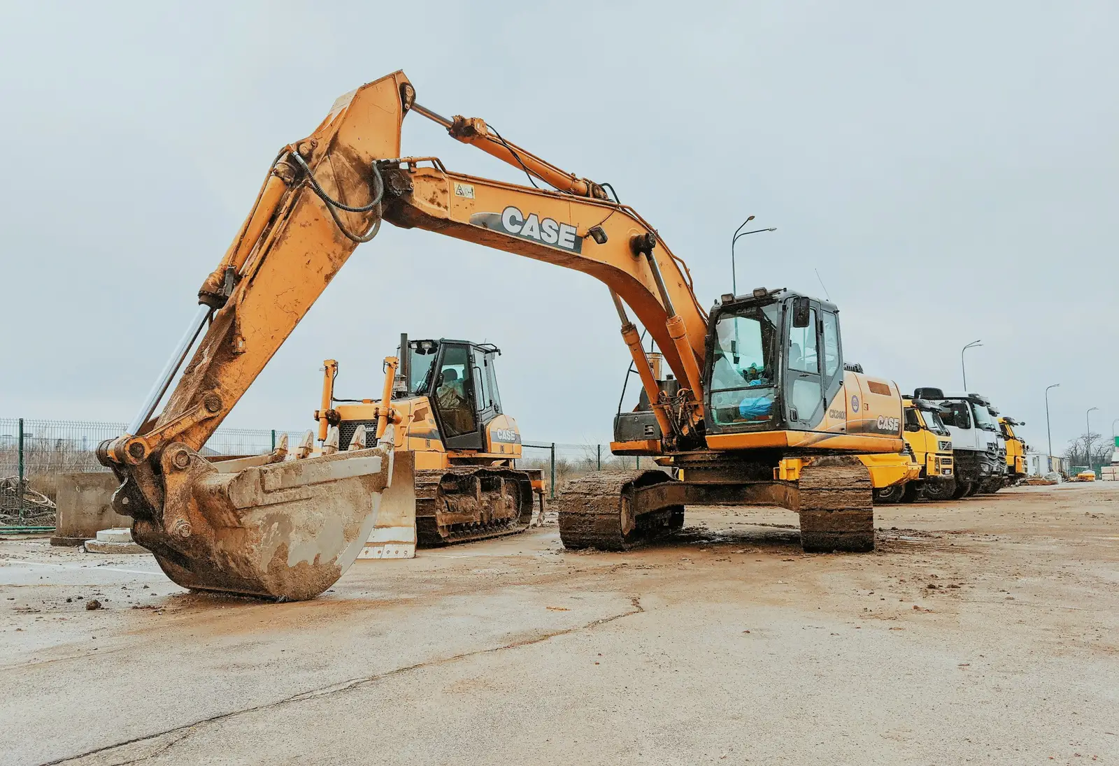 An excavator and a dozer on a concrete yard, with lorries parked in a line behind